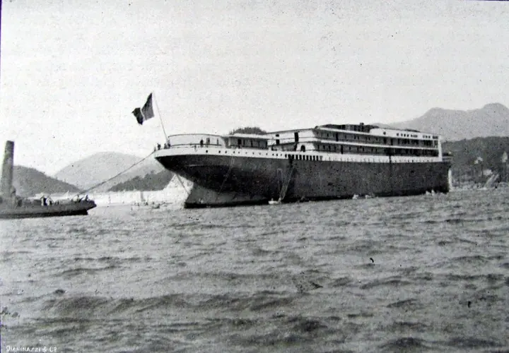The hull already afloat, just after the launch, with the Italian flag at the bow and a tug alongside. The funnels and masts came later.