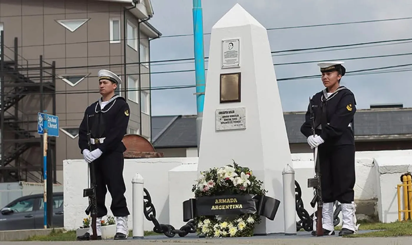 Due marinai della Marina argentina in guardia d’onore davanti a un monumento bianco, con una corona di fiori della Marina.