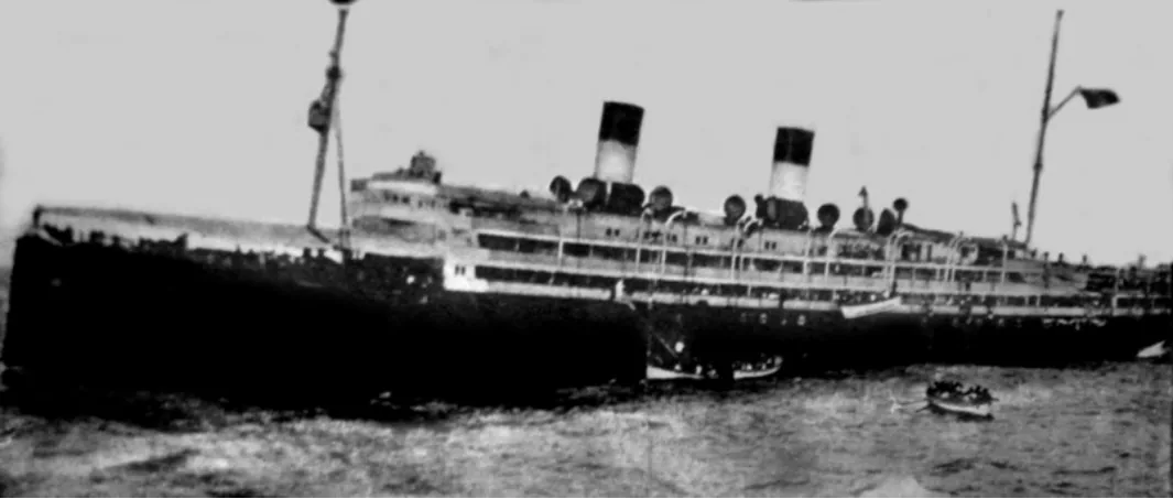 The ship listing, with lifeboats in the water, photographed from the deck of the Alhena.